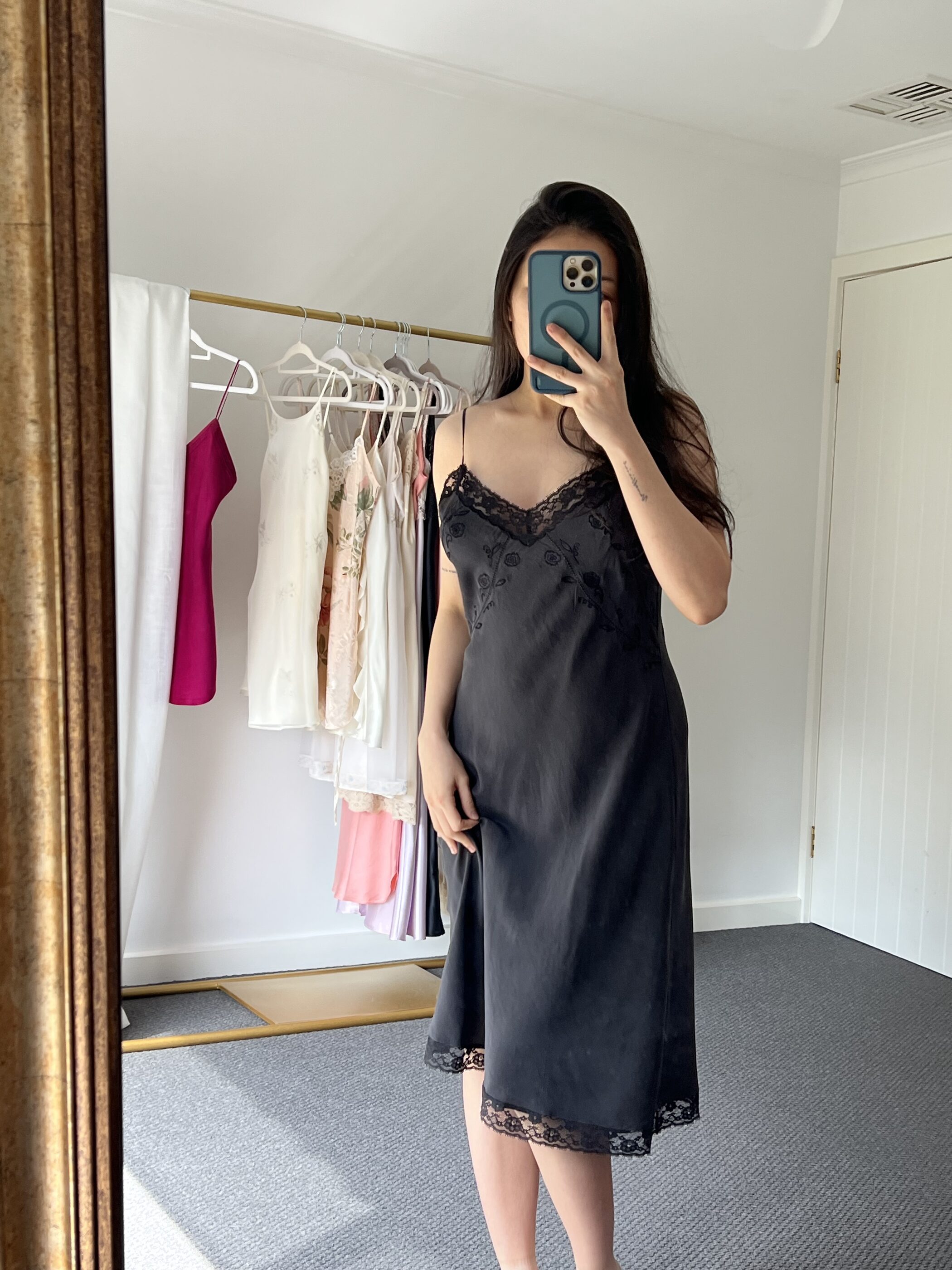 Black silk slip dress with a lace bust and hem, worn, seen in a gilt mirror